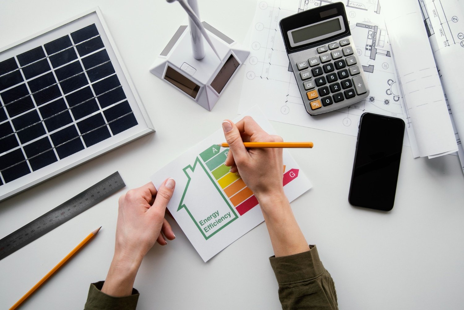 Une personne travaille sur un projet d'évaluation de l'efficacité énergétique, entourée de maquettes de bâtiments et de panneaux solaires.