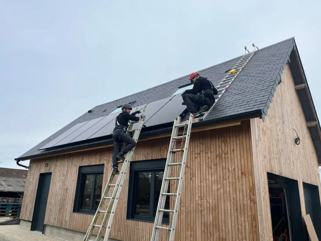 Deux techniciens en tenue de sécurité installent des panneaux solaires sur le toit en bois d'une maison moderne.