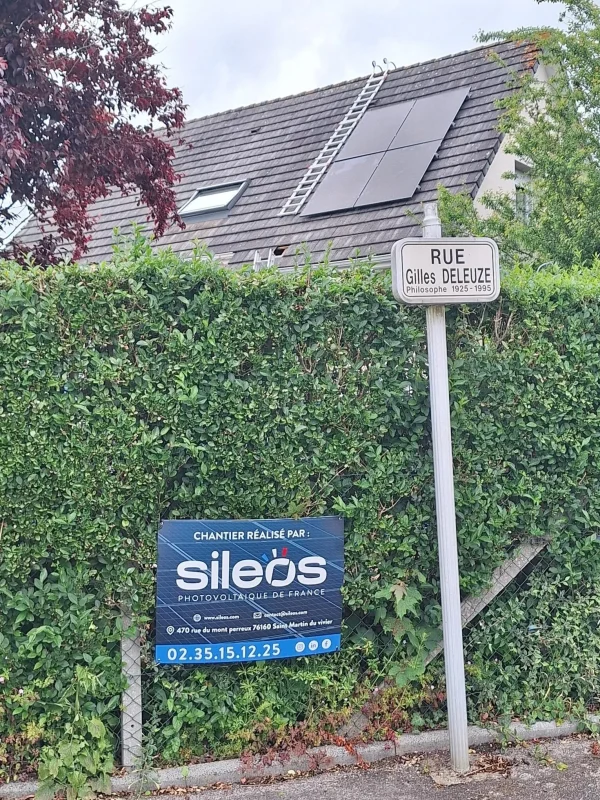 Panneau de rue avec une affiche publicitaire pour des services photovoltaïques sur un fond de haie verte.