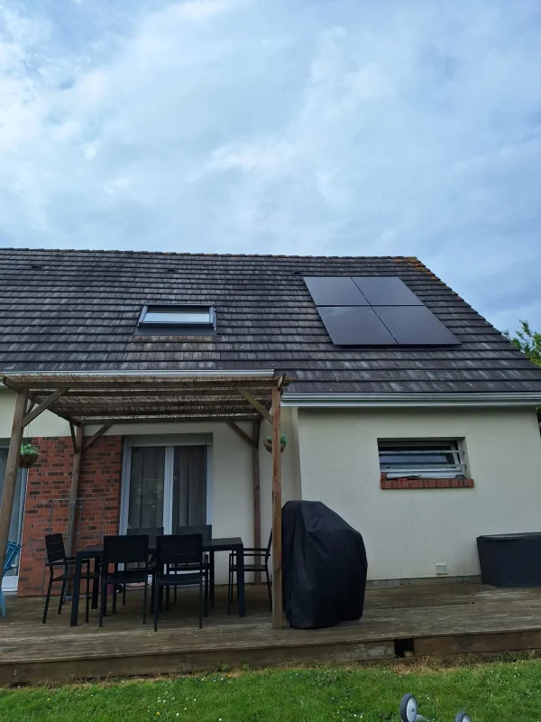Vue d'une maison avec un petit ensemble de panneaux solaires sur le toit, vue de la terrasse avec mobilier de jardin.