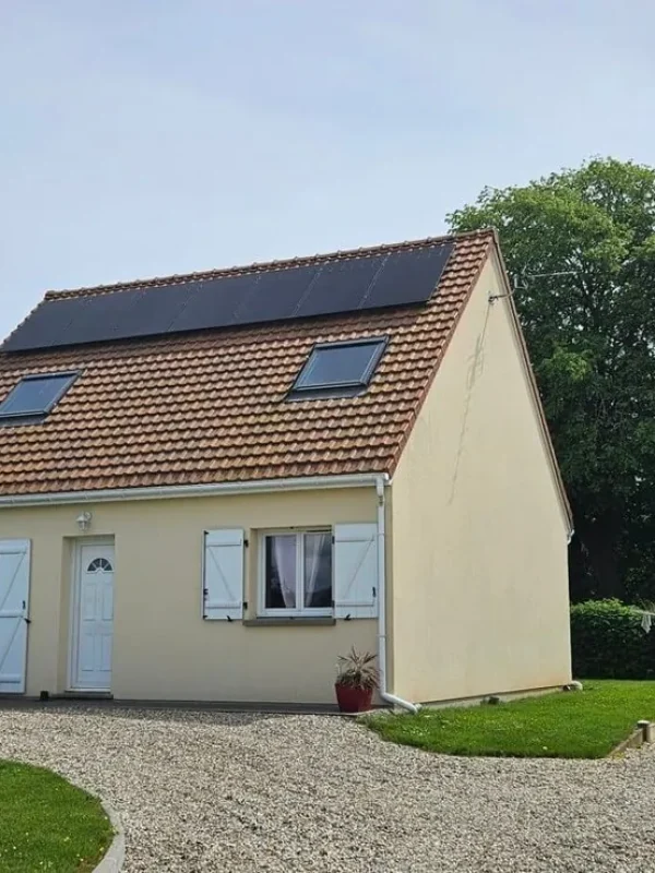 Vue frontale d'une maison avec un chemin de gravier menant à l'entrée, panneaux solaires sur le toit.