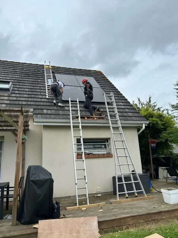 Deux techniciens montent des panneaux solaires sur le toit d'une maison, utilisant des échelles pour accéder au toit.