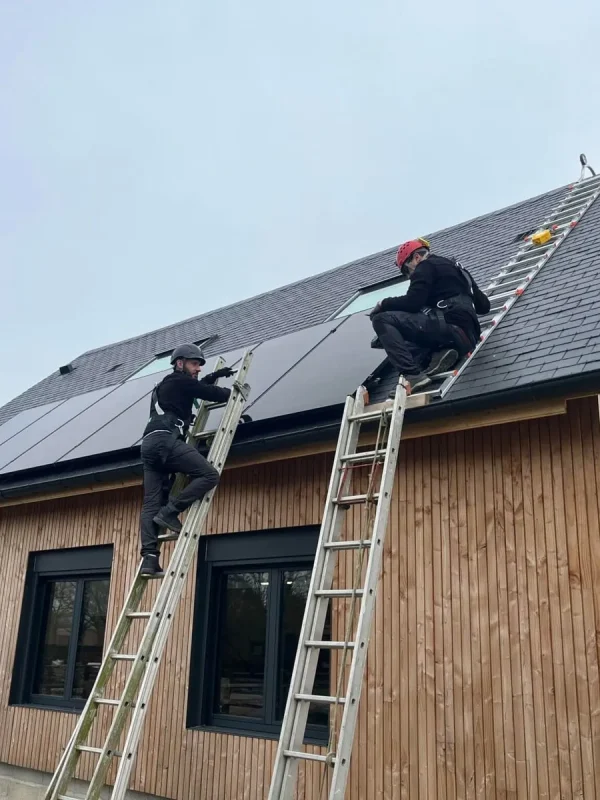 Deux techniciens en tenue de sécurité installent des panneaux solaires sur le toit en bois d'une maison moderne.