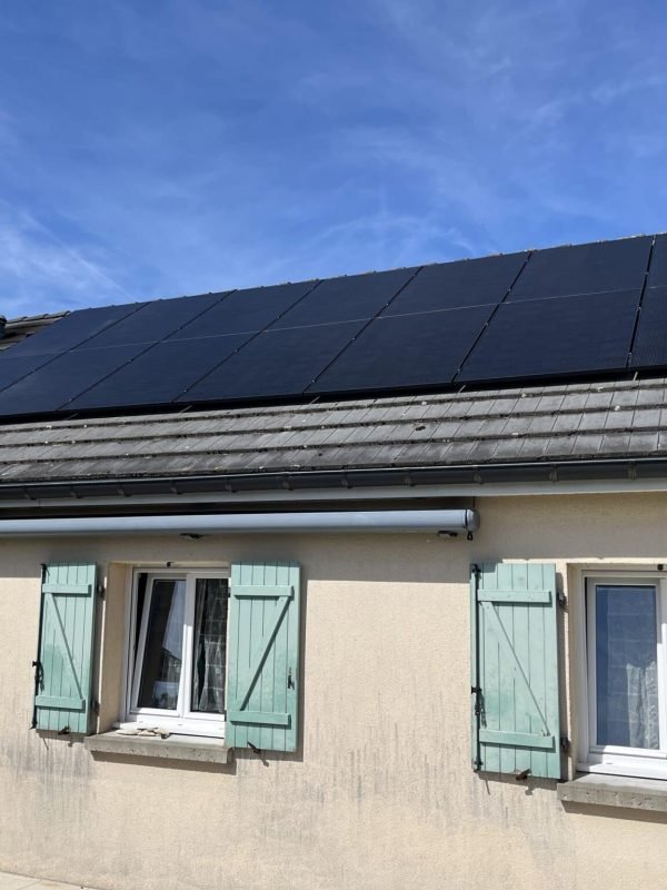 Vue d'une maison résidentielle avec des panneaux solaires couvrant le toit, ciel bleu en arrière-plan et des volets verts aux fenêtres