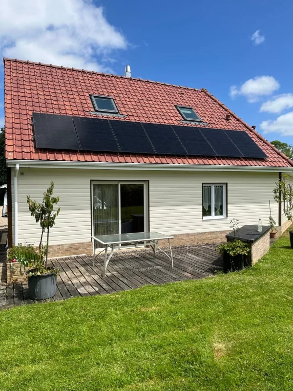 Vue d'une maison moderne avec un grand jardin et une terrasse, toit équipé de panneaux solaires.
