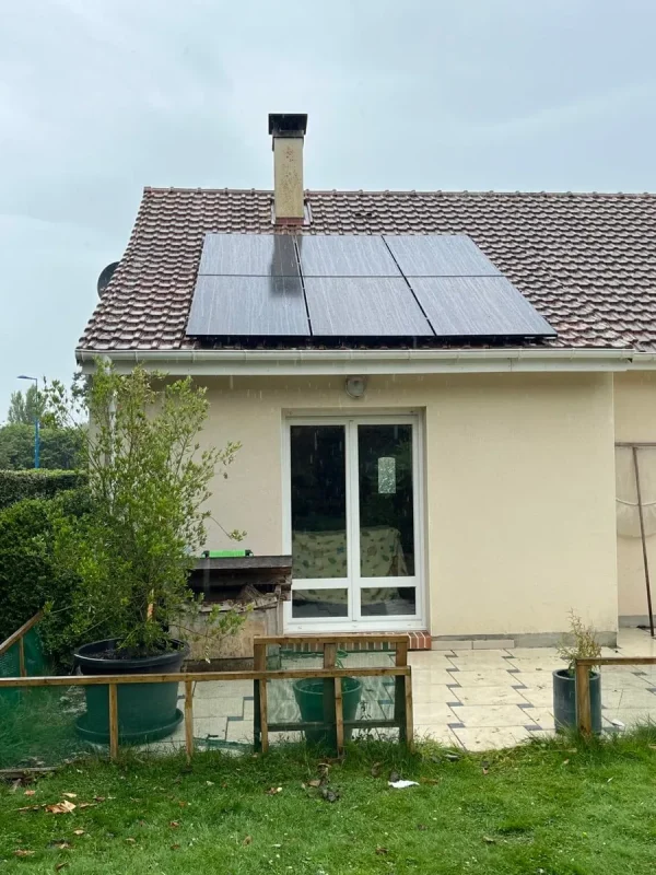 Maison avec un jardin verdoyant sous un ciel nuageux, équipée de panneaux solaires sur le toit.